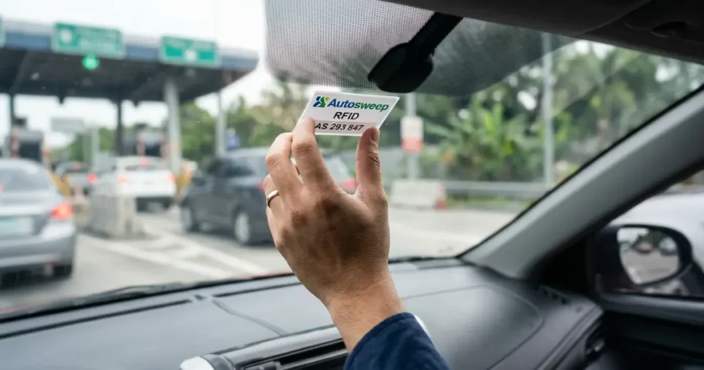 NAIAX Toll Fee Guide in 2026: Complete Rates, Toll Plazas, Autosweep RFID, NAIA Terminals & TRB-Approved Philippines Expressway Details 5 Close-up photograph of Autosweep RFID sticker being installed on the inside of a car windshield in the Philippines, hand pressing white RFID tag near top center of glass for NAIAX Ninoy Aquino International Airport Expressway cashless toll payment SMC Tollways electronic toll collection ETC system 2026